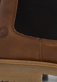 Bruine leren enkelboot met elastische zijpanelen, gestructureerde bovenkant en tan rubberen zool. Heeft een subtiele logo nabij de hak.