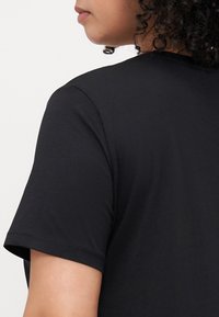 Svart kortärmad t-shirt med rund halsringning, med en mjuk och slät textur. Sömdetaljer synliga vid ärmsluten.