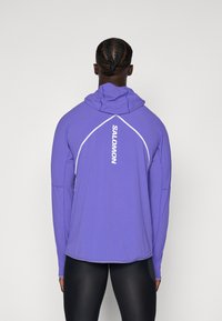 Lila långärmad hoodieskjorta med vit "SALOMON"-logotyp på ryggen och kontrasterande sömdetaljer. Lätt, mjukt tyg.