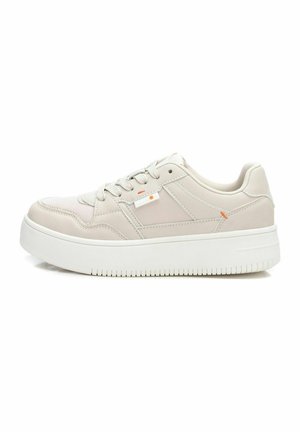 Zapatilla de deporte de color beige claro con parte superior de cuero suave, cuello acolchado, suela de goma blanca y sutiles acentos naranjas. Presenta cordones tradicionales.