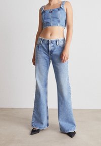 Jeansowy top typu cropped z kwadratowym dekoltem i falbaniastymi ramiączkami, zestawiony z szerokimi jasnoniebieskimi dżinsami. Czarne szpilki w kształcie nosa dopełniają całość.