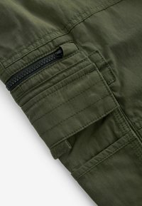 Pantaloni cargo de culoare verde- măslin, dintr-un material texturat, având un buzunar cu fermoar și multiple accente cusute pentru durabilitate.