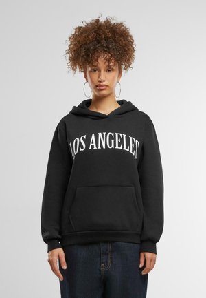 Sudadera negra con "LOS ÁNGELES" impreso en blanco. Cuenta con un bolsillo frontal, capucha con cordón y puños acanalados. Se lleva con jeans oscuros.
