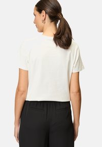 White short-sleeve t-shirt shown from the back, featuring a relaxed fit. Paired with black elastic waistband pants, emphasizing casual wear.