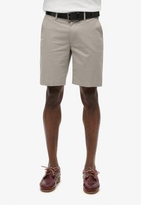 Beige bomuldsshorts med lige snit, der har et sort bælte og bæres med burgunderfarvede læderbådsko med brune snørebånd.