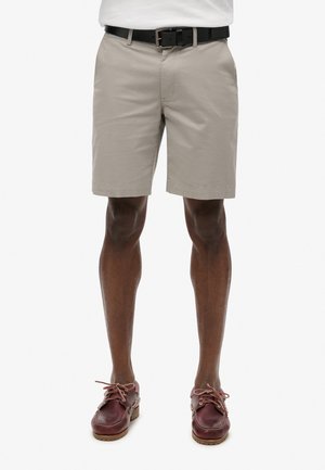 Beige cotton shorts with a straight cut, featuring a black belt, worn with burgundy leather boat shoes and brown laces.