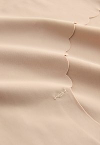 Lichtbeige stof met een gladde textuur, voorzien van golvende randen en subtiele stikdetails.