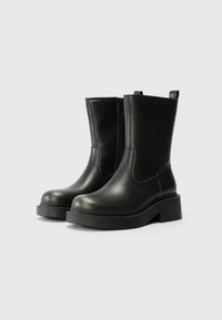 Black leather ankle boots with a smooth finish, side zipper closure, rounded toe, and thick platform sole. Features a pull tab at the back.