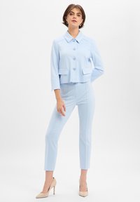 Lichtblauwe cropped jas met knoopsluiting en twee voorzakken, gecombineerd met bijpassende slim-fit broek. Glad stof en op maat gemaakte stijl.