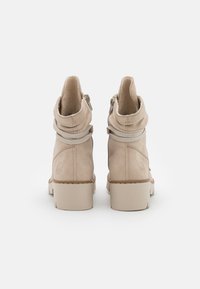 Un paio di stivali beige alla caviglia con tacchi spessi, lacci decorativi avvolti sul retro e cerniere laterali, visti da dietro.