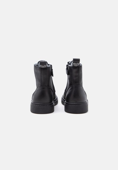 Paire de bottines en cuir noir à semelles épaisses vues de dos, montrant les languettes de tirage et les détails de la fermeture éclair latérale.