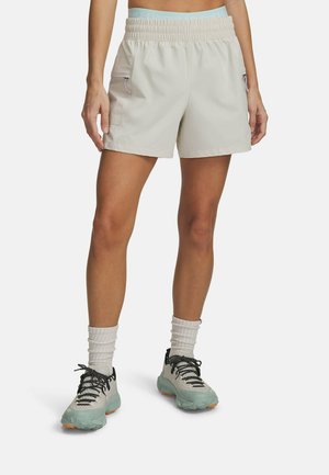 Light beige athletic shorts with an elastic waistband, side zip pockets, and a smooth texture, paired with gray and black hiking shoes.