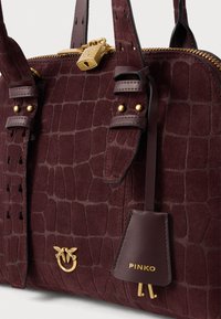 Bordová semišová kabelka s hadím vzorom, zlatým zipsom a zámkom, vtáčím emblémom a koženou visačkou s embosovaným nápisom "PINKO" a pripojenými kľúčmi.