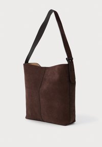 Hnědá semišová taška přes rameno s hladkým povrchem, s jedním nastavitelným koženým popruhem a elegantním, minimalistickým designem.