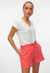 Witte top met korte mouwen, een V-hals en een zigzagpatroon, gecombineerd met koraalkleurige shorts met een elastische tailleband en zijzakken.