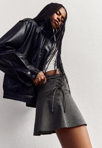 Giacca in pelle nera con dettagli a zip e a scatto, abbinata a una mini gonna grigia a righe con parte frontale con lacci.
