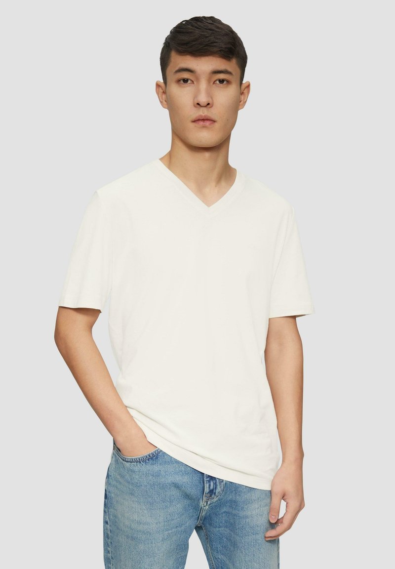 Kurzärmliges, creamfarbendes V-Ausschnitt-T-Shirt aus weichem Stoff. Locker geschnitten und kombiniert mit hellblauen Jeans.