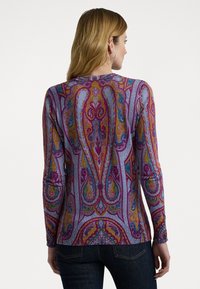 Hosszú ujjú, lila felső, bonyolult paisley mintával arany, rózsaszín és türkiz színekkel. Kerek nyakkivágással és bordázott textúrával rendelkezik.