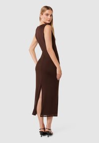 Robe sans manches marron au design ajusté, avec des fentes latérales et une texture lisse. Associée à des talons noirs pour un look complet.