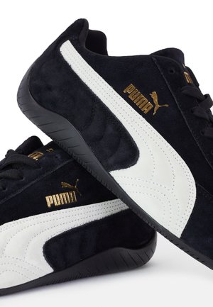 Baskets Puma en daim noir avec bandes blanches sur les côtés, semelles noires, lacets noirs et logo Puma doré sur les côtés et la languette.