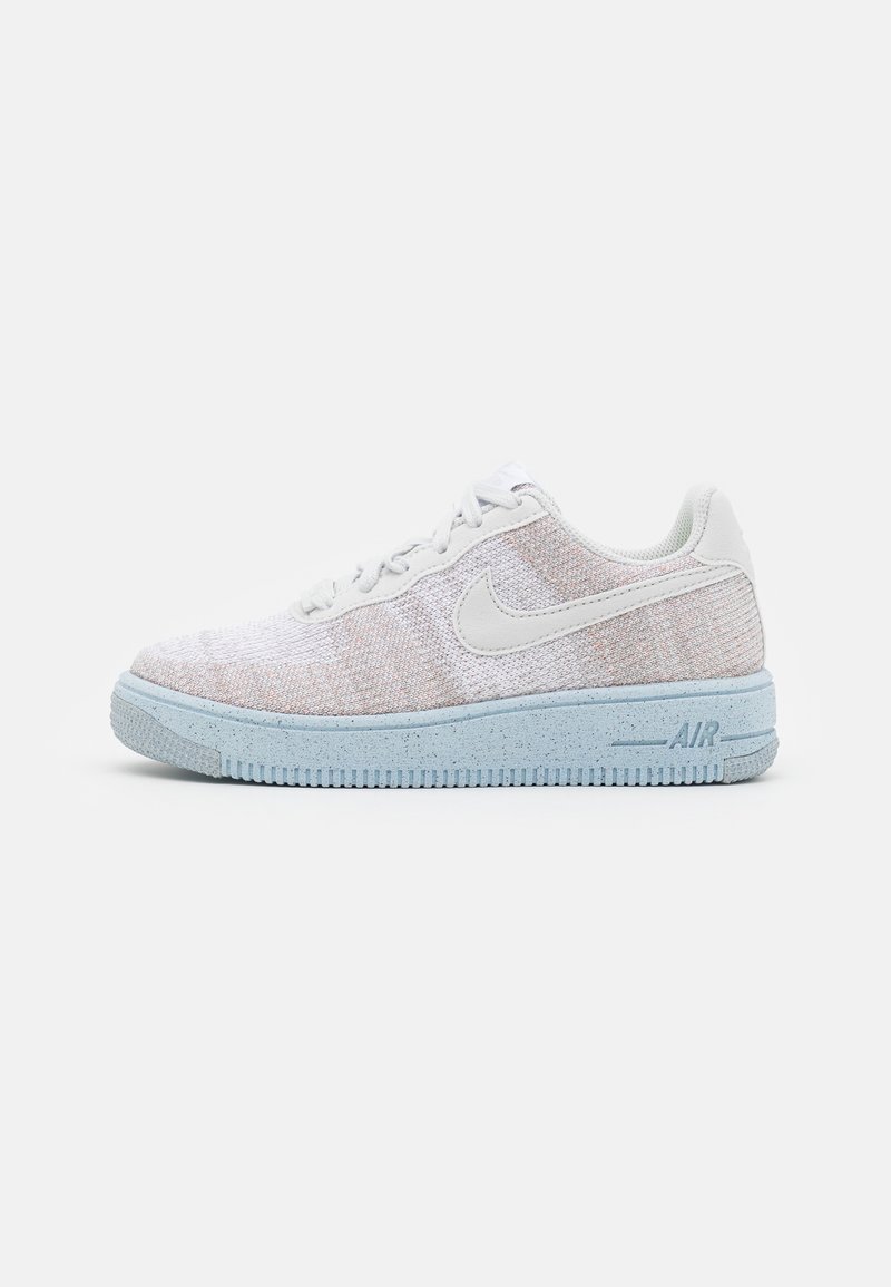 Sneaker basse Nike Air avec tige en maille blanche, logo swoosh blanc et semelle bleu clair tachetée, présenté en vue latérale sur fond blanc.