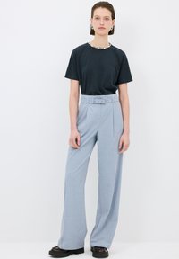 Donker t-shirt met een decoratieve halslijn, gecombineerd met lichtblauwe hoog-geplaatste broeken met een riem en wijde pijpen, aangevuld met zwarte schoenen.