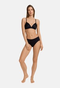 Reggiseno nero senza cuciture a forma triangolare con spalline sottili, abbinato a slip neri a vita alta. Texture liscia, design minimalista.