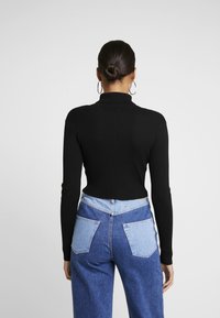 Zwarte geribbelde coltrui met lange mouwen, gecombineerd met high-waisted blauwe denim jeans met contrasterende lichtblauwe zakken.
