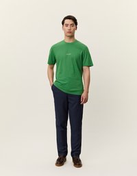 Groene katoenen T-shirt met ronde hals en korte mouwen, gecombineerd met donkerblauwe broek. Bruine leren schoenen maken de look compleet.
