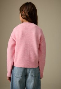 Maglione rosa lavorato a maglia con vestibilità comoda, orlo a coste e spalle scese, abbinato a jeans in denim azzurro chiaro. Texture morbida e tonalità calda.