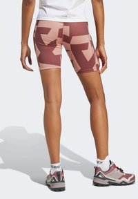 Brown and pink patterned athletic shorts made of stretchy material, featuring a fitted design and smooth texture, paired with hiking shoes.