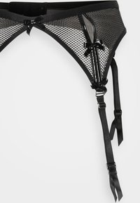Sort mesh strumpebånd med satinbuer, justerbare stropper og skinnende accenter. Har et semi-gennemsigtigt design og tekstureret mønster.