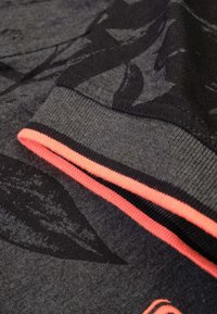 Donkergrijze sweatshirt met een zwart bladenpatroon, voorzien van een ribbelmanchet met een contrasterende neonroze rand. Zachte textuur met gemengde stoffen.