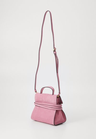 Rozā zamšādas rokassoma ar garu regulējamu siksnu, noapaļotu rokturi un dekoratīvu pārsietu detaļu. Iezīmē struktūru un melnas akcentus.