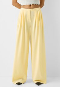 Wide-leg trousers in light yellow fabric, featuring front pleats and a single button closure. Smooth texture and a relaxed fit.