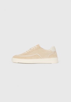 Beige ruskinds sneakers med hvid sål og snørebånd, lavtop design og zigzag mønster på sålen.