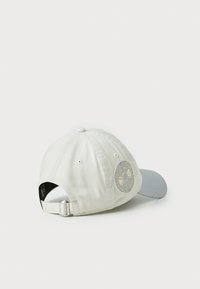 Hvid bomulds cap med en buet grå skygge. Har et broderet cirkulært design på siden og et metaljusteringsrem bagpå.