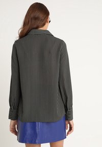 Schwarzgestreifte Hemdbluse mit langen Ärmeln, mit Kragen und abgerundetem Saum. Getragen mit einem blauen Leder-Minirock.