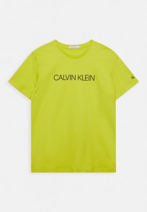 Camiseta de manga corta de color amarillo-verde brillante con "CALVIN KLEIN" impreso en negro en el pecho y un pequeño logo "ck" en la manga izquierda.