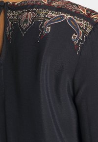 Marinebluse mit glatter textur, ausgestattet mit buntem Paisleymuster-Stickerei entlang des Ausschnitts und der Schulterpartie.
