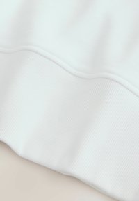 Nærbillede af hvidt stof, der viser ribbet struktur og sømdetalje ved kanten, hvilket antyder en manschet eller sømkant på et beklædningsstykke.