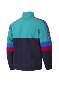 Kleurgeblokte jas gemaakt van lichtgewicht stof. Bevat teal, marineblauw, rood en blauwe panelen met logo-details op de mouwen en een elastische onderkant.