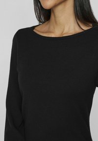 Top nero a maniche lunghe con scollatura tonda, realizzato in un materiale lavorato a maglia morbido. Presenta un design aderente e una texture liscia.