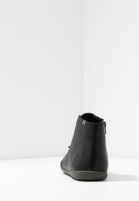 Černá kožená kotníková bota s hladkou texturou, se zipem a kulatou špičkou. Podešev je mírně zvýšená, poskytující oporu.