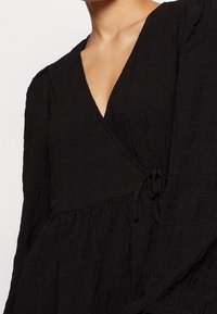 Svart omlotkjol med långa ärmar, texturerat tyg, djup v-ringning och knytning i midjan.