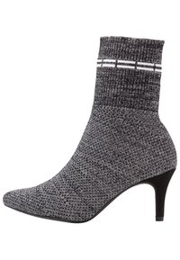 Bottines en tricot noires et grises avec un bout pointu et un talon de 7,5 cm. Présentent des accents rayés en haut et un tissu texturé.