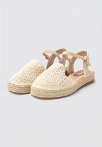 Espadrilles tejidas en beige con punta redonda, correa en el tobillo y suela texturizada. Presenta un acento decorativo en el lateral.