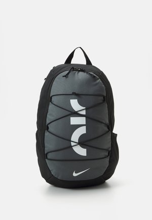 Mochila Nike en poliéster gris y negro, con logo blanco, detalles de cordón elástico y tirantes acolchados para mayor comodidad. Diseño compacto.