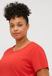 Punainen lyhythihainen t-paita, joka on valmistettu puuvillasta, pyöreällä pääntiellä ja pienellä Levi's-tunnuksella vasemmassa rinnassa. Sileä pinta.