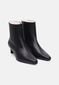 Bottines noires en cuir avec un bout pointu et un petit talon carré. Elles possèdent une fermeture éclair sur le côté et une texture lisse.